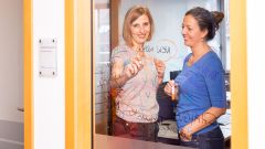 Zwei Frauen schreiben auf eine Glaswand, das Wort „NEW WORK“ steht im Zentrum.