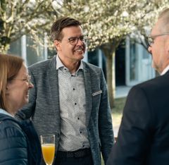 Drei Personen im Gespräch bei einer Outdoor-Veranstaltung, ein Mann hält ein Glas mit Orangensaft.