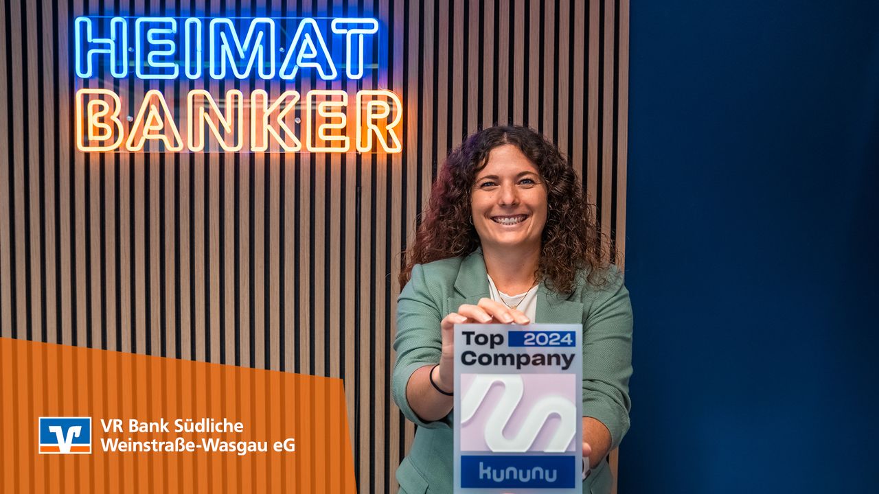 Frau hält Kununu-Siegel „Top Company 2024“ vor „HEIMAT-BANKER“-Leuchtschrift der VR Bank Südliche Weinstraße-Wasgau.