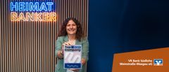 Frau hält Kununu-Siegel „Top Company 2024“ vor „HEIMAT-BANKER“-Leuchtschrift der VR Bank Südliche Weinstraße-Wasgau.