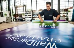 Mitarbeiter aus der Konfektionierung wickelt ein großes Werbeplakat auf