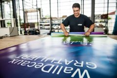 Ein Mitarbeitender wickelt ein großes Werbeplakat auf.