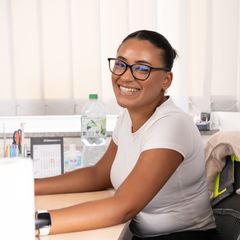 Mitarbeiterin an ihrem Schreibtisch lächelt in Kamera