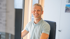 Büro Mitarbeiter an seinem Arbeitsplatz lächelt in die Kamera