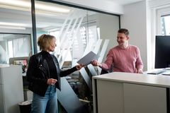 Eine Mitarbeiterin übergibt einem Kollegen Dokumente